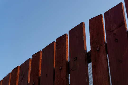 A simple fence made of red planks on which the sun shines against a blue sky.
