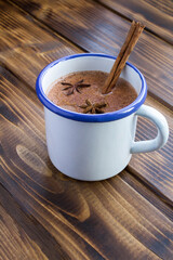 Hot cocoa with cinnamon in the white metal mug  on the wooden background. Location vertical.