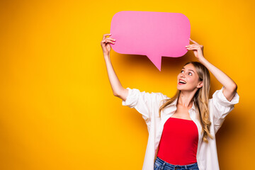 Portrait of a happy young woman holding empty speech bubble standing over yellow background