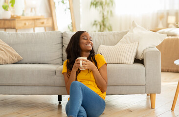 Obraz premium Quiet morning times with coffee. Young black lady drinking hot aromatic beverage on floor at home