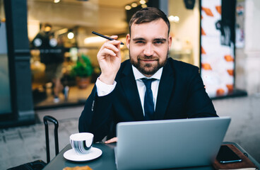Half length portrait of formally dressed businessman 30s sitting at sidewalk table in street cafe...