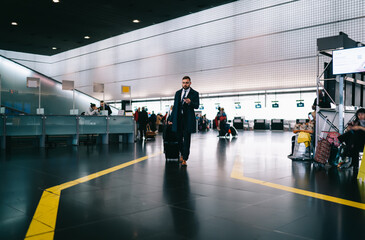 Entrepreneur walking with luggage using mobile phone for checking departure gate at airport...