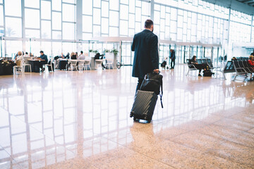 Back view of formally dressed businessman in coat hurry up to flight departure in airport, male...