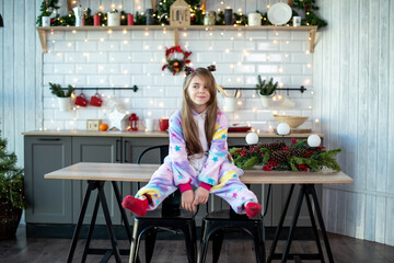 smiling toddler girl sets in the Christmas kitchen on table , Christmas decorations, lights, new year fun