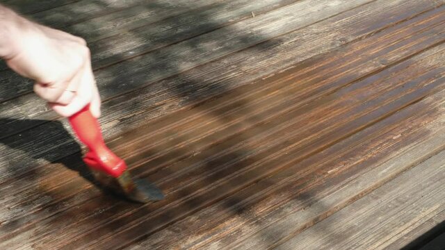 A man holds a paint brush in his hand and paints the floor. Close-up.