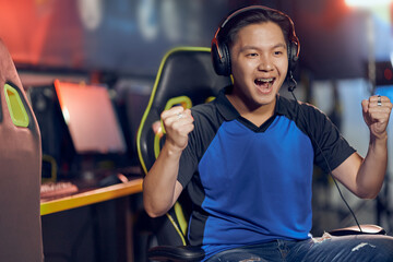 Winning. Portrait of excited asian guy, male cyber sport gamer wearing headphones looking at PC screen and celebrating success while participating in eSports tournament