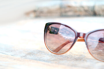 Closeup image of femalle brown sunglasses at sea yellow sand background.