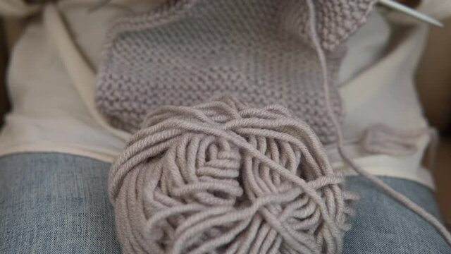 Knitting time at home. A view of a female hands knitted a grey wool in the house.