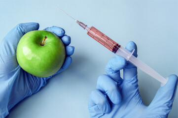 Green apple and syringe with GMO in hands on a blue background.