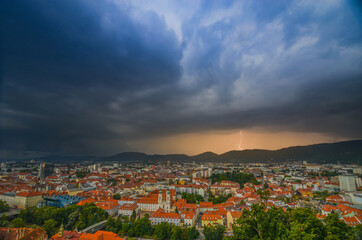 Fototapeta premium Lightning storm with dramatic clouds over the city of Graz, with Mariahilfer church and historic buildings, in Styria region, Austria