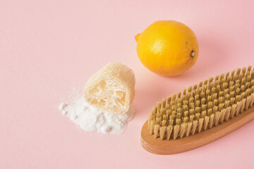 soda spilled, loofah, lemon and wooden cleaning brush on pink background