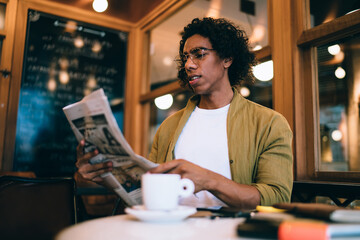 Bewildered man reading newspaper while drinking coffee in cafe