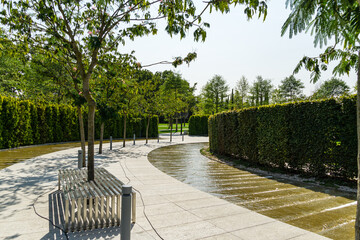 City park Krasnodar. Artificial swift river with granite banks runs around evergreen hedge with rest area. Public landscape 'Galitsky park' for relaxation and walking in sunny autumn September 2020