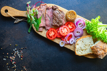 meat sandwich and vegetables burger loaf of bread, tomato, lettuce, medium or rare steak on the table serving size top view copy space for text food background rustic