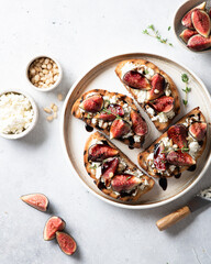 bruschetta with figs, cream cheese, balsamic sauce and pine nuts in a ceramic plate on a light background, top view