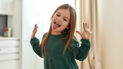 A small happy girl playing around emotionally smiling with her tongue out and her hands raised with...