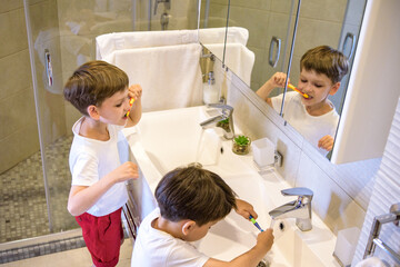 Older brother learning to clean the teeth for younger brother in the bathroom with mirror