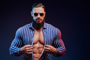 Succesful and muscular bearded guy showing his perfect abs and posing in dark background.