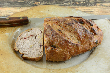 Loaf of cranberry walnut bread and slice with bread knife on large serving plate on table