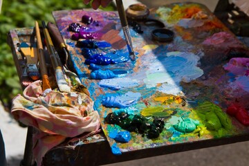 artist wooden palette, mess of fresh bright colorful oil paints mixed in disorder, outdoor painting plein air, author hand hold a paintbrush, creative vibrant inspiration postcard