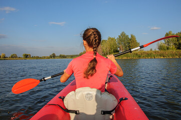 A girl in a pink T-shirt is rowing in a kayak on a calm river. Ukraine