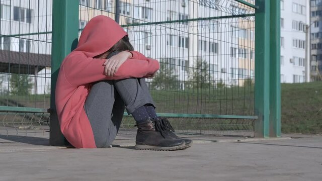 The child is depressed. Childhood loneliness. A depressed girl sits on the floor in the street.