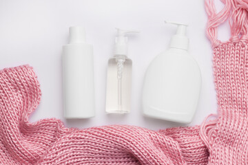 Obraz na płótnie Canvas Winter care cosmetics set. White bottles next to a pink knitted scarf