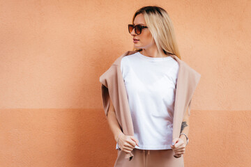 Stylish blonde girl wearing white t-shirt and glasses posing against street