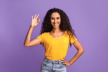 It's OK. Cheerful young brunette woman gesturing okay sign over purple background