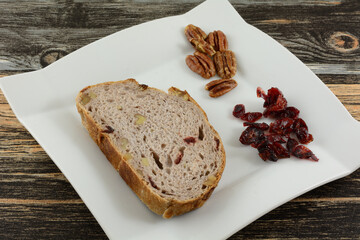 Slice of cranberry walnut bread with nuts and dried cranberries on table