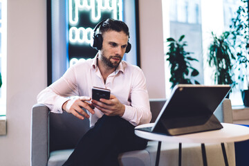 Caucasian businessman in earphones watching video webinar using bluetooth on touch pad and...