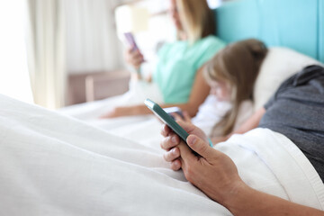 Family man woman child lie in bed and everyone holds smartphone in their hands. Family dependence on gadgets concept