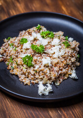 Buckwheat salad of fried onion, cottage cheese and parsley served on a black plate on a wooden table