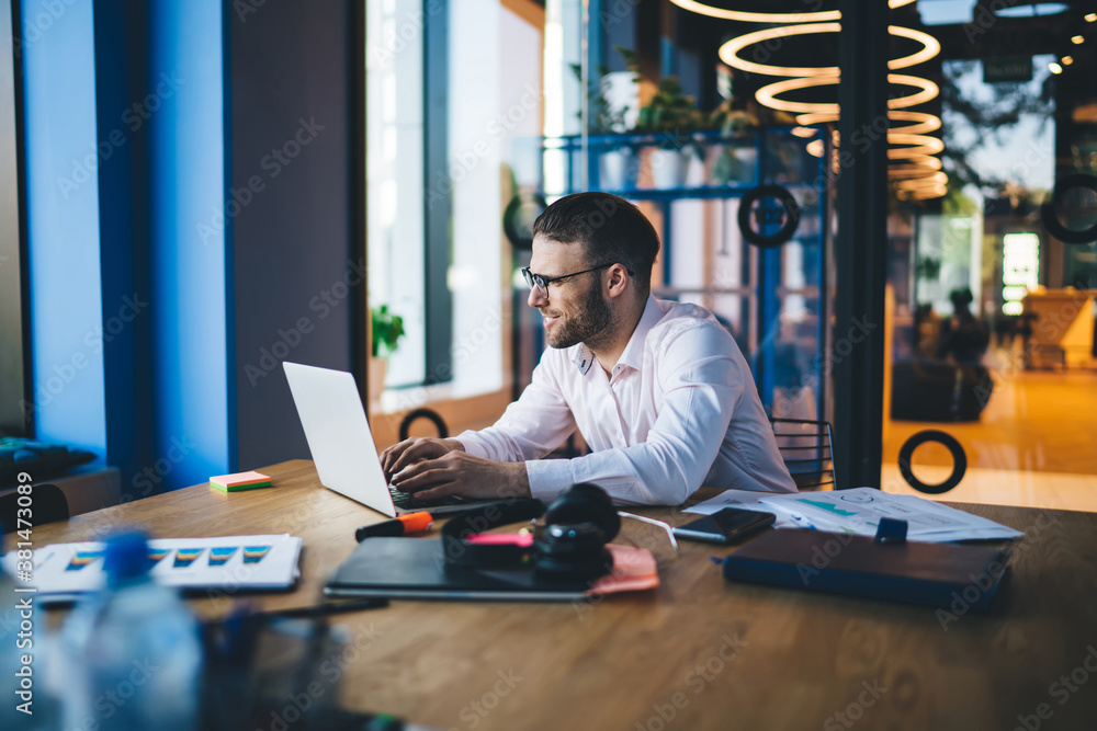 Poster successful office worker in classic spectacles browsing banking website for making web booking, happ