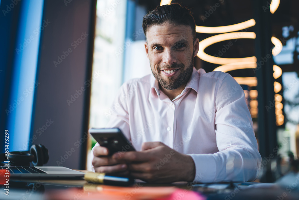 Poster portrait of millennial caucasian freelancer smiling at camera enjoying mobile networking via modern 