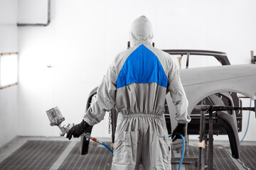 rear view on young adult auto mechanic holding machine for polishing and cleaning, painting of cars. unrecognizable guy in protective uniform stand ready to work, in the service