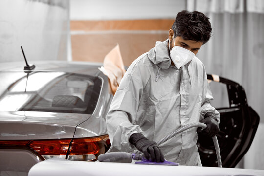 young caucasian bearded car cleaner in respirator and protective glasses polishing car with polish machine, in uniform. isolated in car service