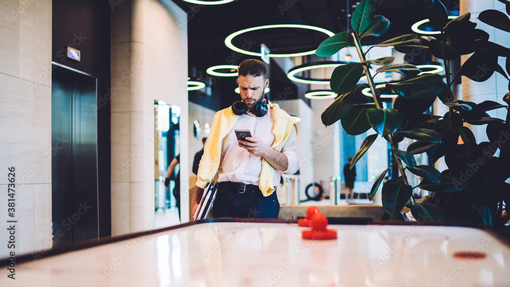 Poster caucasian male coworker with earphones using internet connection in workspace with air hockey table 