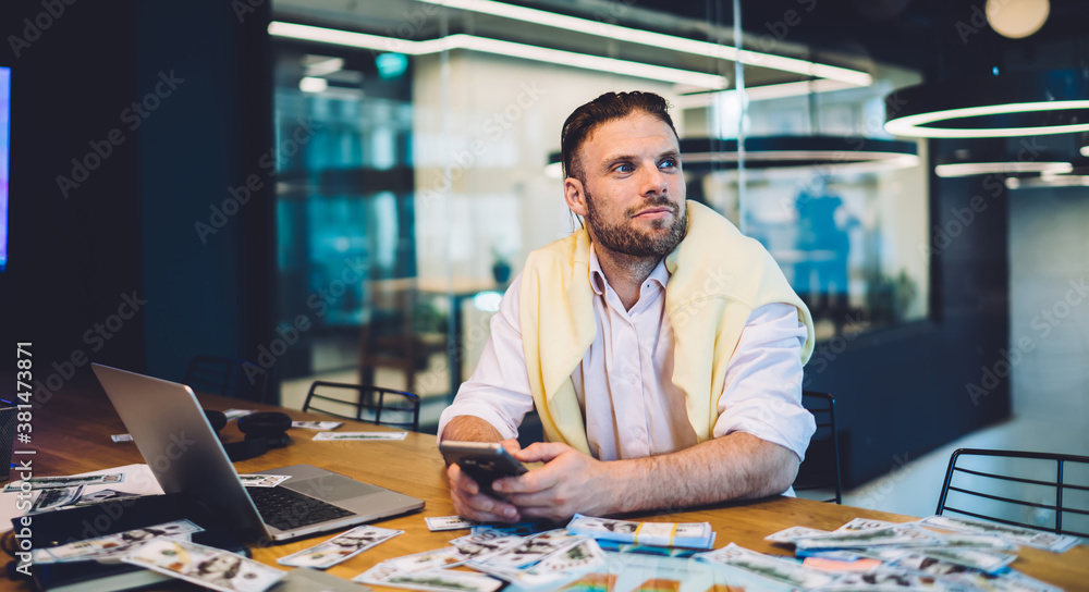 Poster contemplative male trader with smartphone and netbook pondering on exchange offer on stock website, 