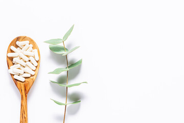 Collagen capsules in the wooden spoon and aromatic eucalyptus twig on white background. Minimalism...