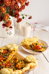 Pie with vegetables, yeast dough with pre-stewed vegetables and cheese baked in the oven, white table with pie and plate with fork, flowers in a vase