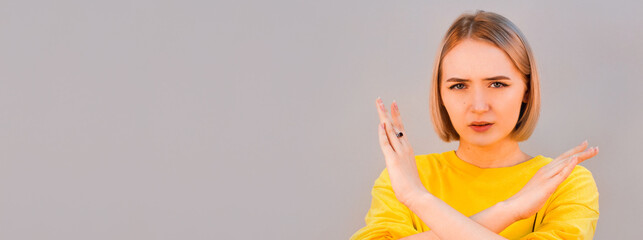 Angry serious european woman showing crossed hands gesture and looking at camera while standing isolated over gray background