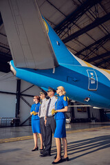 Happy smiling flight team wearing their respective black and blue uniforms standing near the hangar at the airport