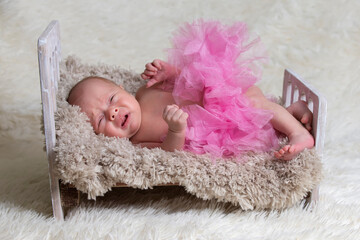 Newborn baby crying in the crib.Baby in a pink skirt on a fur bed.