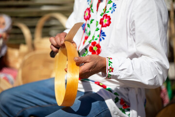A Slavic man in an embroidered shirt makes products from birch bark.