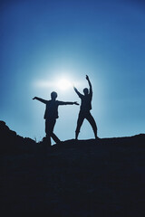 Dark silhouettes of a young couple of a guy and a girl of travelers on the top of the mountain indulge and rejoice against the background of the sun