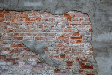 Front view of an old, dirty and weathered wall. Gray plastering is broken revealing old bricks. High resolution full frame textured background.