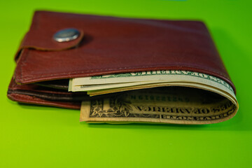 Partmone with paper dollar bills lies on a green background.