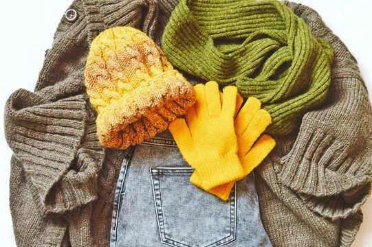 Flat lay photography fall and winter fashion clothes. Brown cardigan, gray jeans, yellow hat, gloves and green woolen scarf. Top view photo autumn wardrobe items