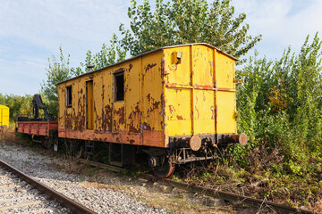 Fototapeta na wymiar Old yellow train with big holes, rusty and abandoned in the field on the old tracks